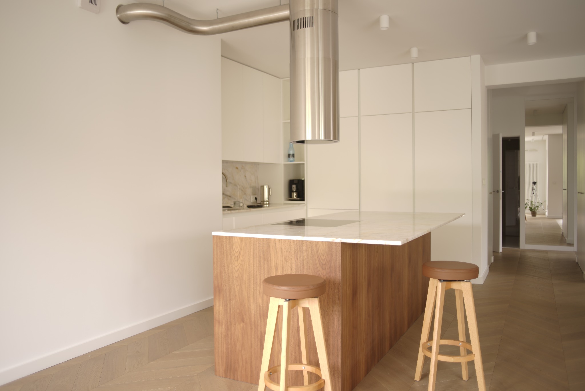 Nowoczesna kuchnia z wyspą o drewnianym wykończeniu i marmurowym blatem, uzupełniona o minimalistyczne hokery i designerski okap.