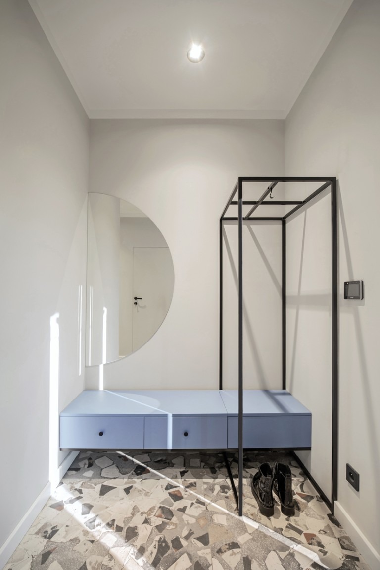 Nowoczesny przedpokój w Sosnowcu: błękitna szafka z szufladami, okrągłe lustro i metalowy wieszak na tle mozaikowej podłogi. Minimalistyczny design.