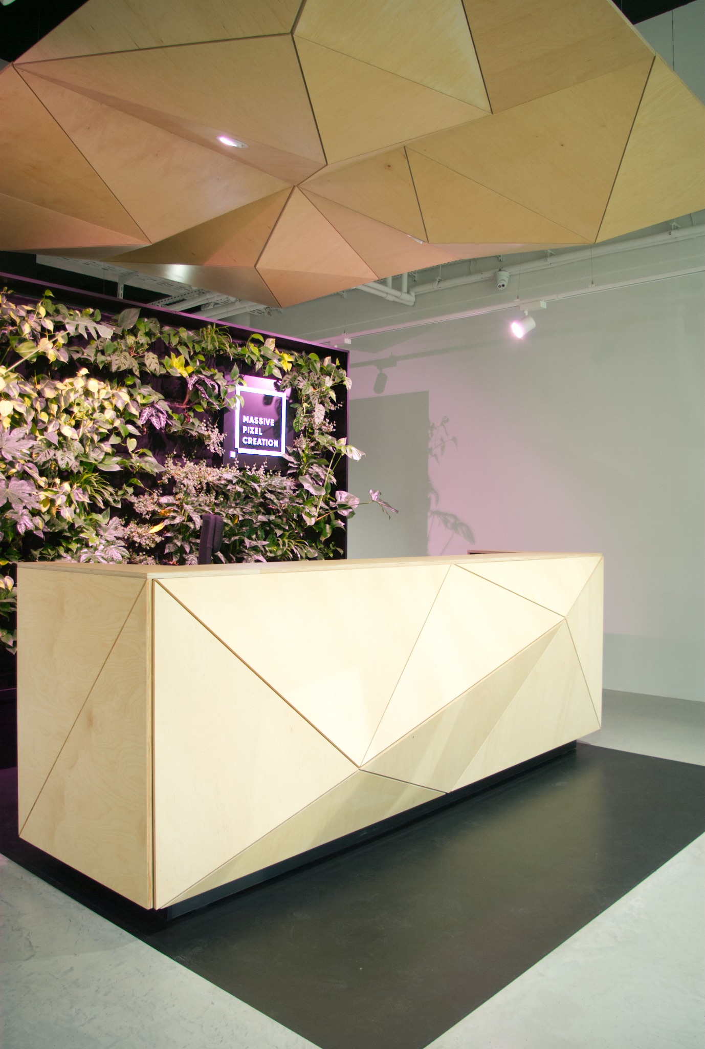 Nowoczesna recepcja z drewna z geometrycznym wzorem, podświetlona ściana z roślin i designerski sufit z trójkątnych paneli. Minimalistyczne wnętrze.