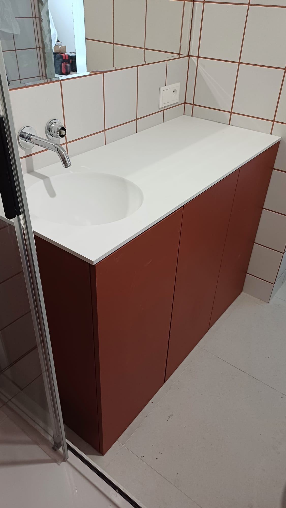 Nowoczesna szafka łazienkowa z umywalką w kolorze terakoty, biały blat, chromowana bateria, płytki na ścianie z brązową fugą. Minimalistyczny design.