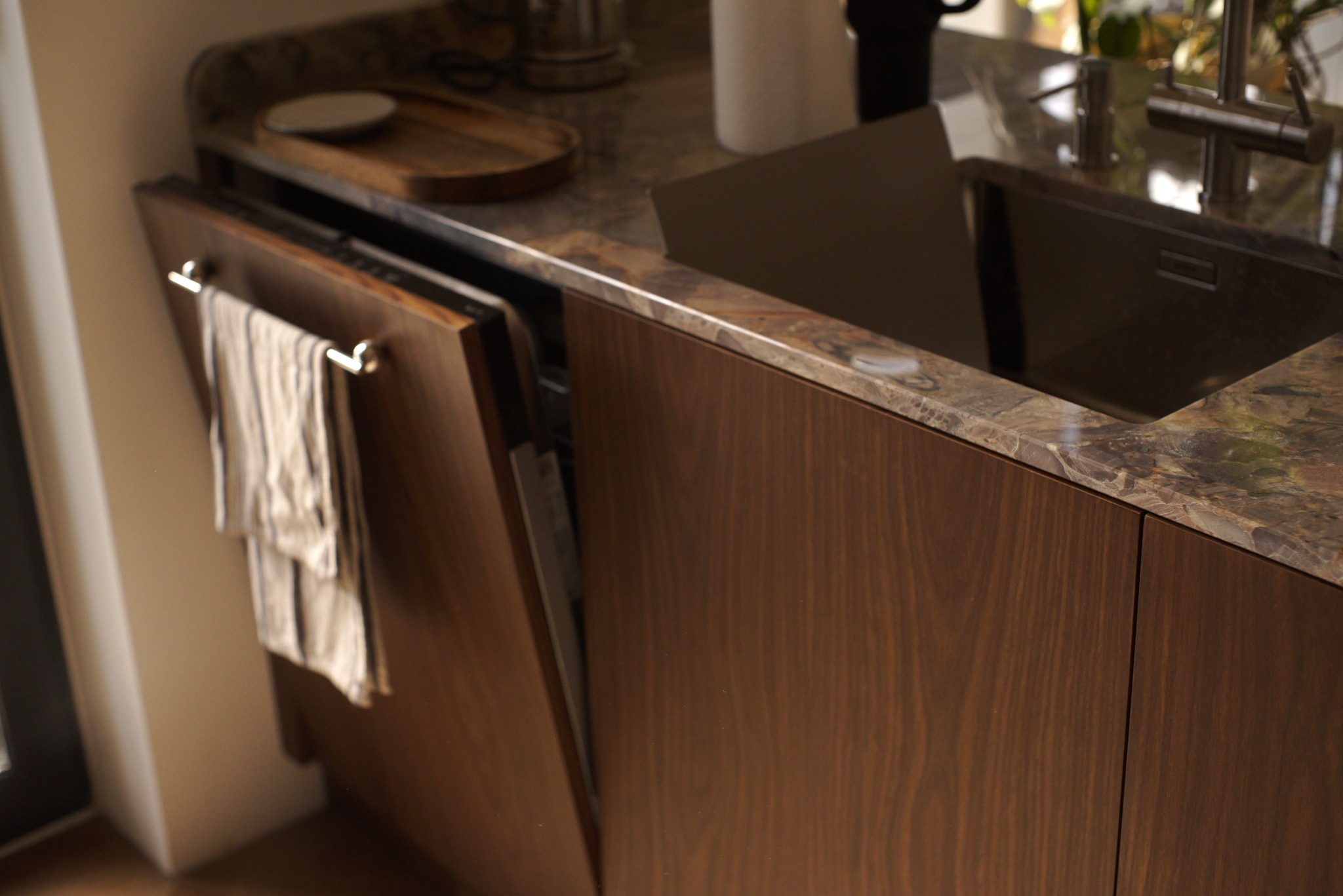 Nowoczesna zabudowa kuchenna z drewnianymi frontami i marmurowym blatem. Otwarta szafka z relingiem na ręcznik. Widoczny zlew i bateria.