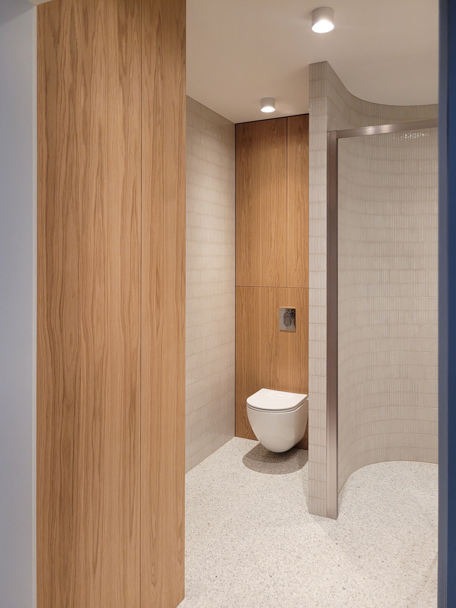 Nowoczesna łazienka z drewnianą zabudową, podwieszaną toaletą i mozaiką na ścianach. Jasne wnętrze z akcentami drewna i minimalistycznym designem.