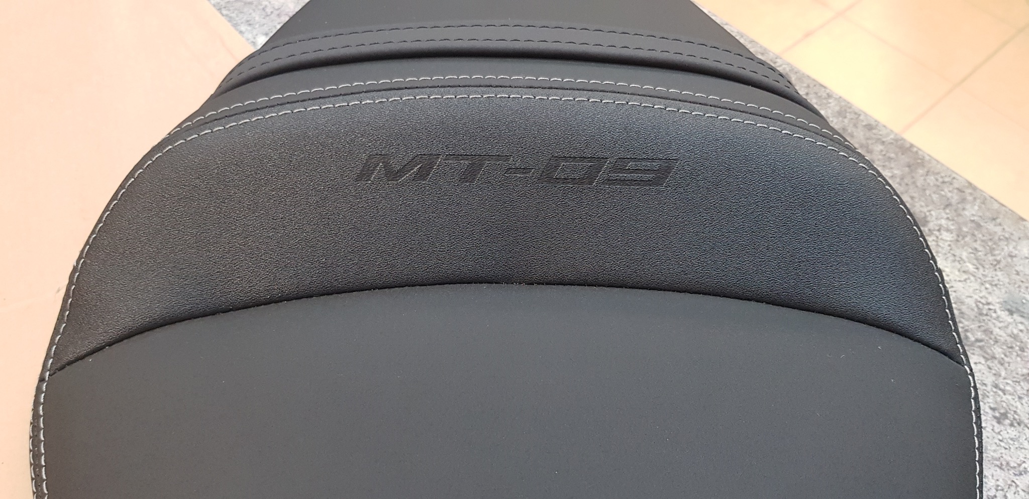 Czarne, odnowione siedzenie motocyklowe z białymi przeszyciami i wytłoczonym logo MT-09, prezentujące precyzję wykonania i dbałość o detale.