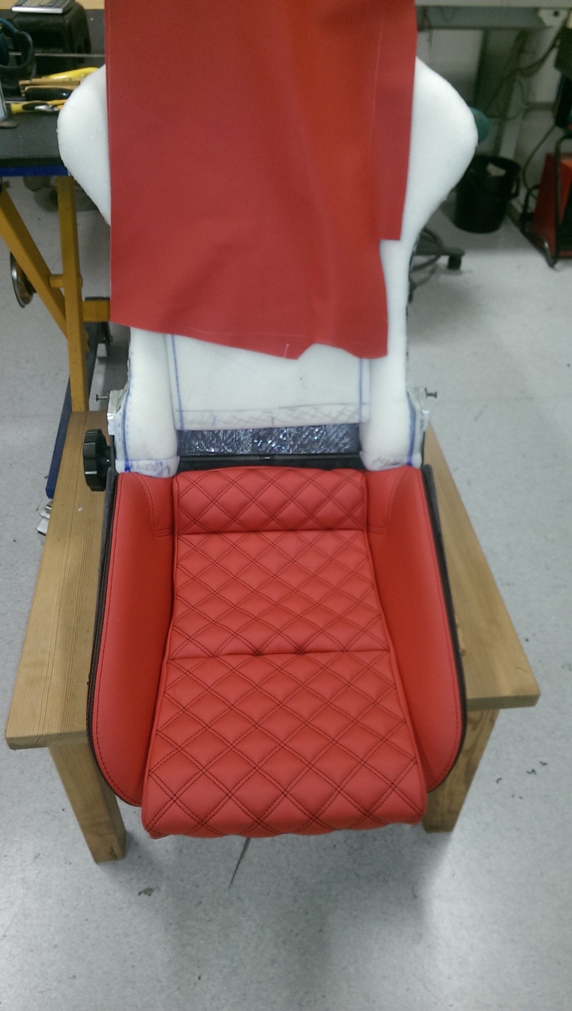Czerwone, pikowane siedzisko samochodowe w trakcie tapicerowania we Wrześni. Widoczna pianka i materiał przygotowany do montażu. Detal wykończenia.