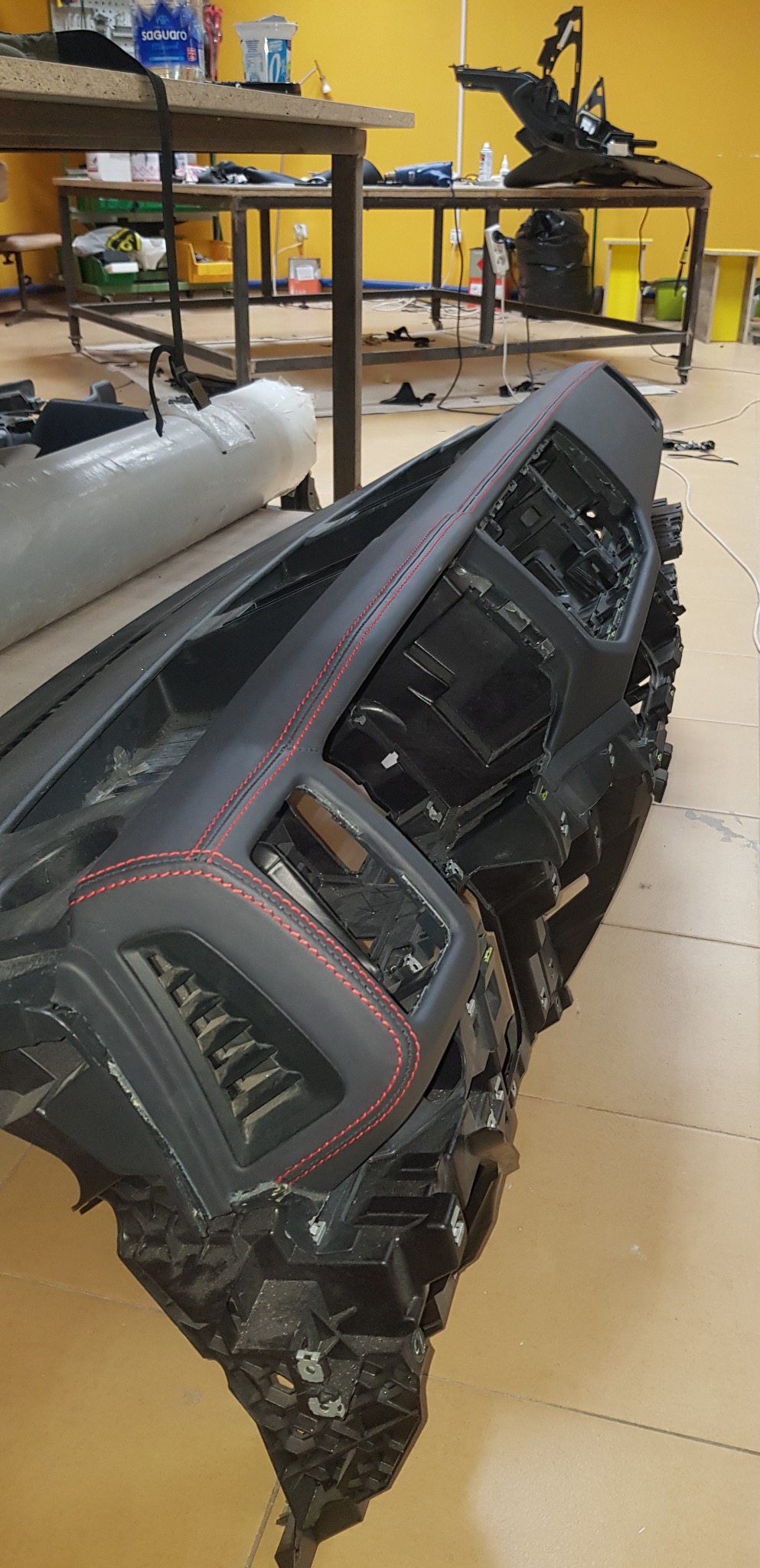 Deska rozdzielcza samochodu po renowacji tapicerskiej, obszyta czarną skórą z czerwonymi przeszyciami, widoczna w warsztacie tapicerskim.