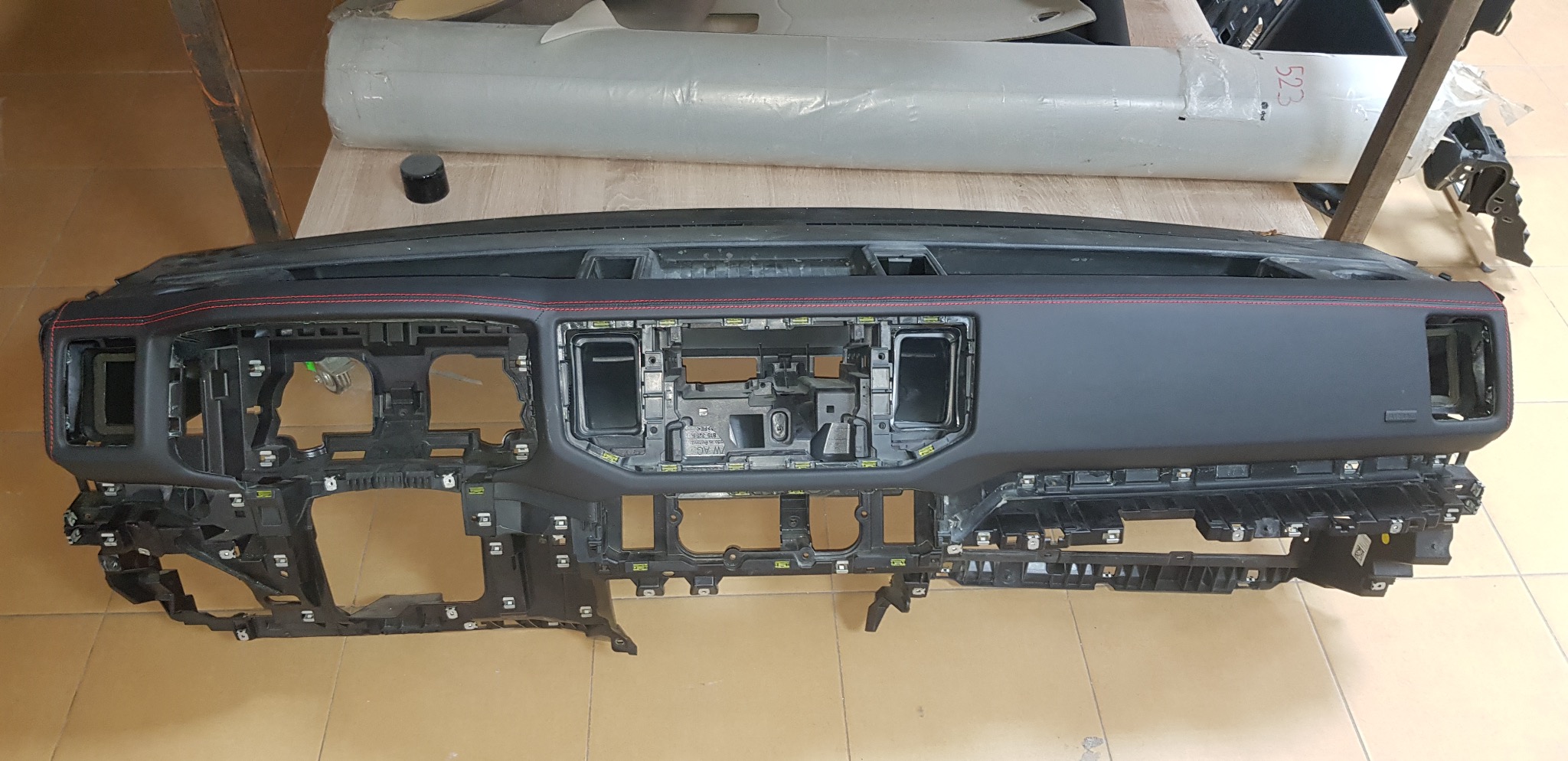 Deska rozdzielcza samochodu po obszyciu czarną skórą z czerwonymi przeszyciami, widoczna na warsztatowym stole. Elementy montażowe i konstrukcja deski rozdzielczej.