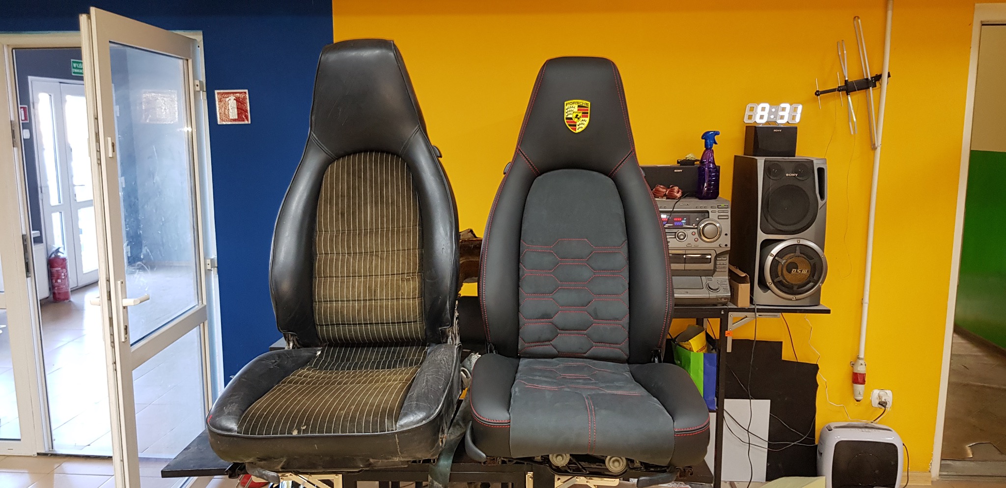Porównanie: zniszczony fotel samochodowy obok odnowionego, czarnego fotela z czerwonymi przeszyciami i logo Porsche. Widoczne różnice w tapicerce i ogólnym stanie.
