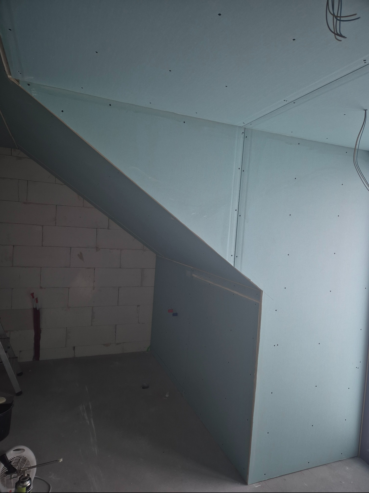 Płyty gipsowo-kartonowe na poddaszu, widoczne łączenia i śruby, surowy stan wykończenia, fragment ściany z pustaków, widok z dołu.