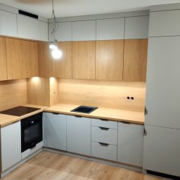 EA studio - Jasna kuchnia z drewnianymi akcentami: szare szafki dolne i górne, drewniany blat, płyta indukcyjna i piekarnik. Minimalistyczny design z oświetleniem punktowym.