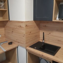 Koliber Studio - Częściowo wykończona kuchnia z drewnianymi panelami, czarnym zlewem i widocznymi narzędziami, sugerująca etap montażu lub wykończenia.