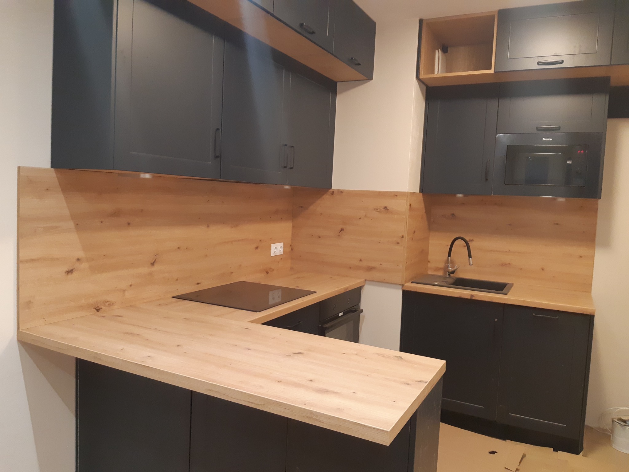 Nowoczesna kuchnia w Stalowej Woli: grafitowe szafki z drewnianym blatem i panelem. Minimalistyczny design, zabudowa kuchenna z piekarnikiem i płytą indukcyjną.