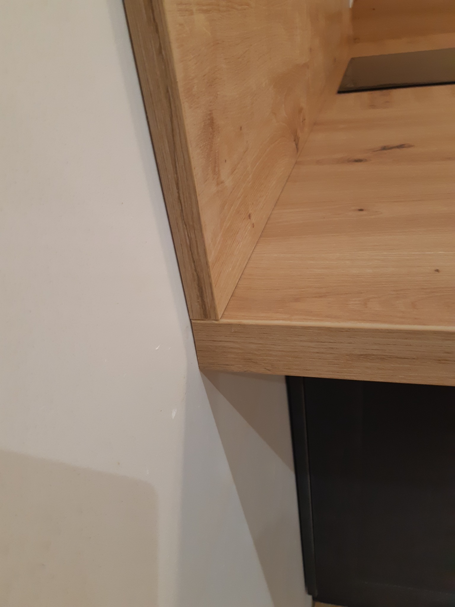 Fragment blatu z drewna dębowego, zamontowanego przy ścianie, z widocznym frontem szafki w kolorze czarnym. Detal wykończenia wnętrza.