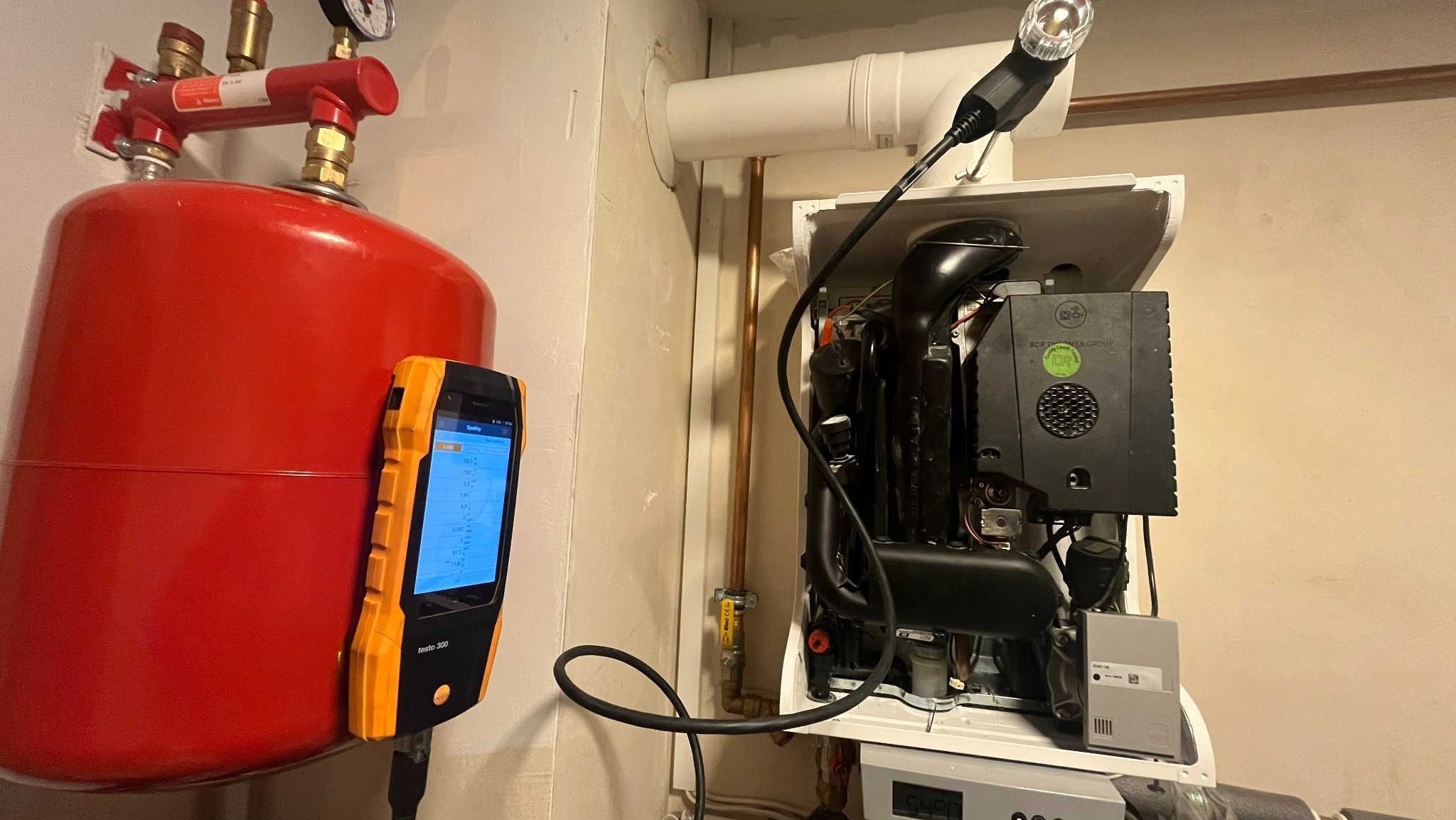 Czerwony zbiornik ciśnieniowy, analizator spalin Festo 300 i piec gazowy z widocznymi rurami miedzianymi. Kontrola szczelności instalacji.