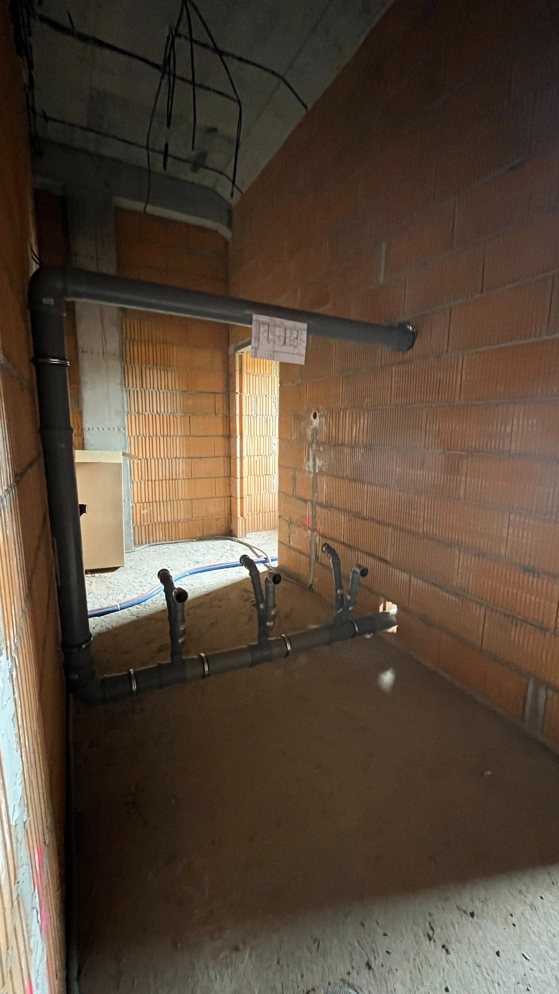 Szare rury kanalizacyjne z podłączeniami w surowym wnętrzu z ceglanymi ścianami. Widoczne elementy instalacji przed wykończeniem.