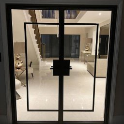 Dmytro Marienko - Nowoczesne, dwuskrzydłowe drzwi wejściowe z czarną, geometryczną ramą, widok na elegancki hol z marmurową podłogą i schodami. Minimalistyczny design.