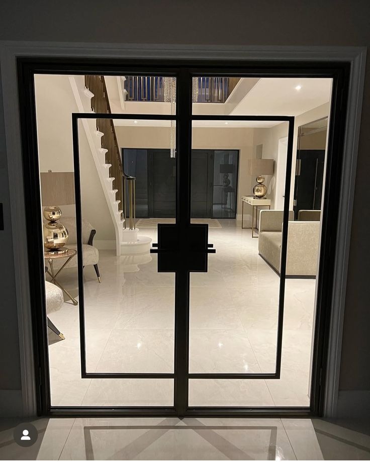 Nowoczesne, dwuskrzydłowe drzwi wejściowe z czarną, geometryczną ramą, widok na elegancki hol z marmurową podłogą i schodami. Minimalistyczny design.