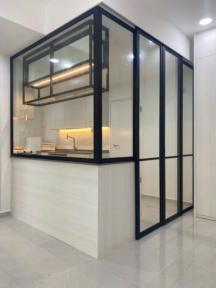 Nowoczesna, przeszklona konstrukcja z czarnymi profilami oddzielająca kuchnię, z widocznym oświetleniem LED i blatem. Minimalistyczny design, jasne wnętrze.