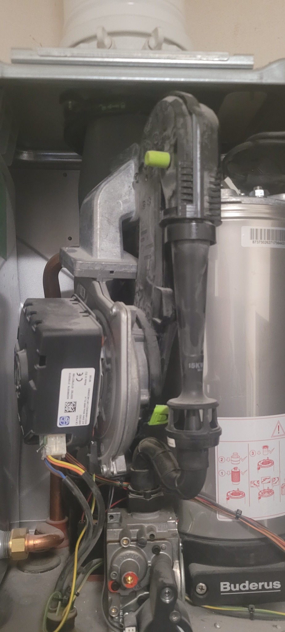 Wnętrze kotła gazowego Buderus z widocznymi elementami instalacji, w tym rurami miedzianymi i czarnymi przewodami. Detal techniczny, bliski kadr.