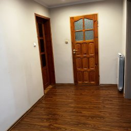 Pogotowie Stolarskie WoodCraft Marcin Krawczyk - Korytarz z panelami podłogowymi o wzorze drewna, widoczne dwie drewniane ościeżnice i drzwi. Grzejnik przy ścianie. Jasne ściany i sufit z oświetleniem punktowym.