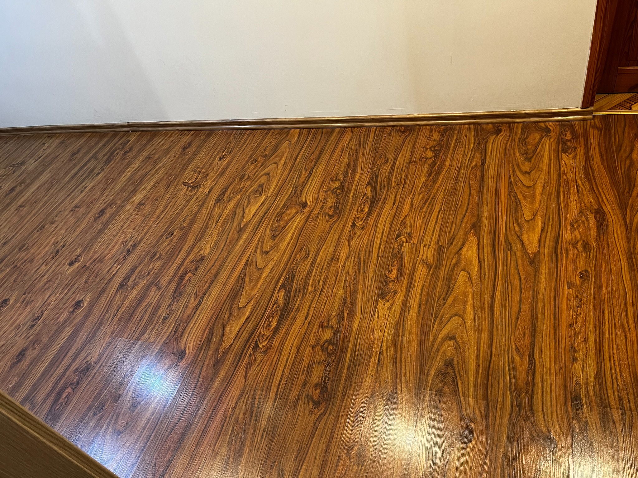 Ukończona podłoga z paneli o wzorze drewna, z widocznymi listwami przypodłogowymi i fragmentem ściany. Układanie paneli z dbałością o detale.