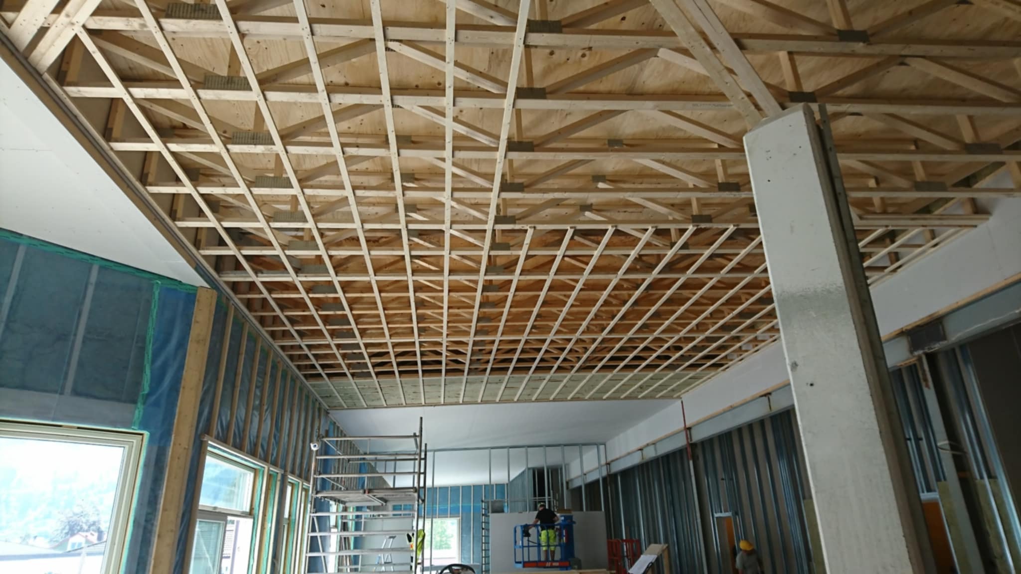 Szkielet sufitu podwieszanego z drewnianych łat, widoczny z dołu, w trakcie prac w Lublinie. Metalowe profile ścian i rusztowanie w tle.