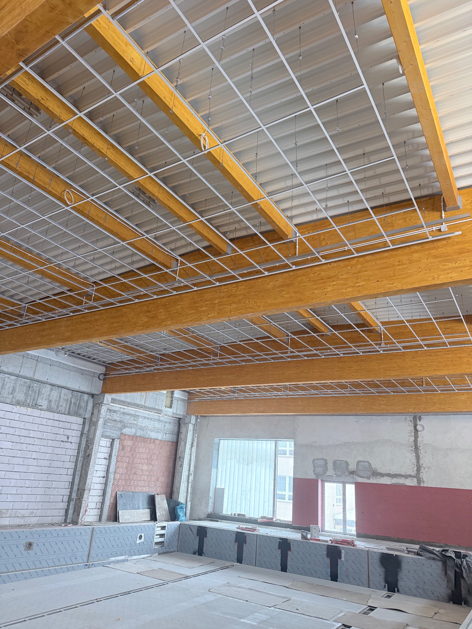 Montaż sufitu podwieszanego z drewnianymi belkami w Olsztynie. Widoczna konstrukcja i elementy instalacji w nowym budynku.