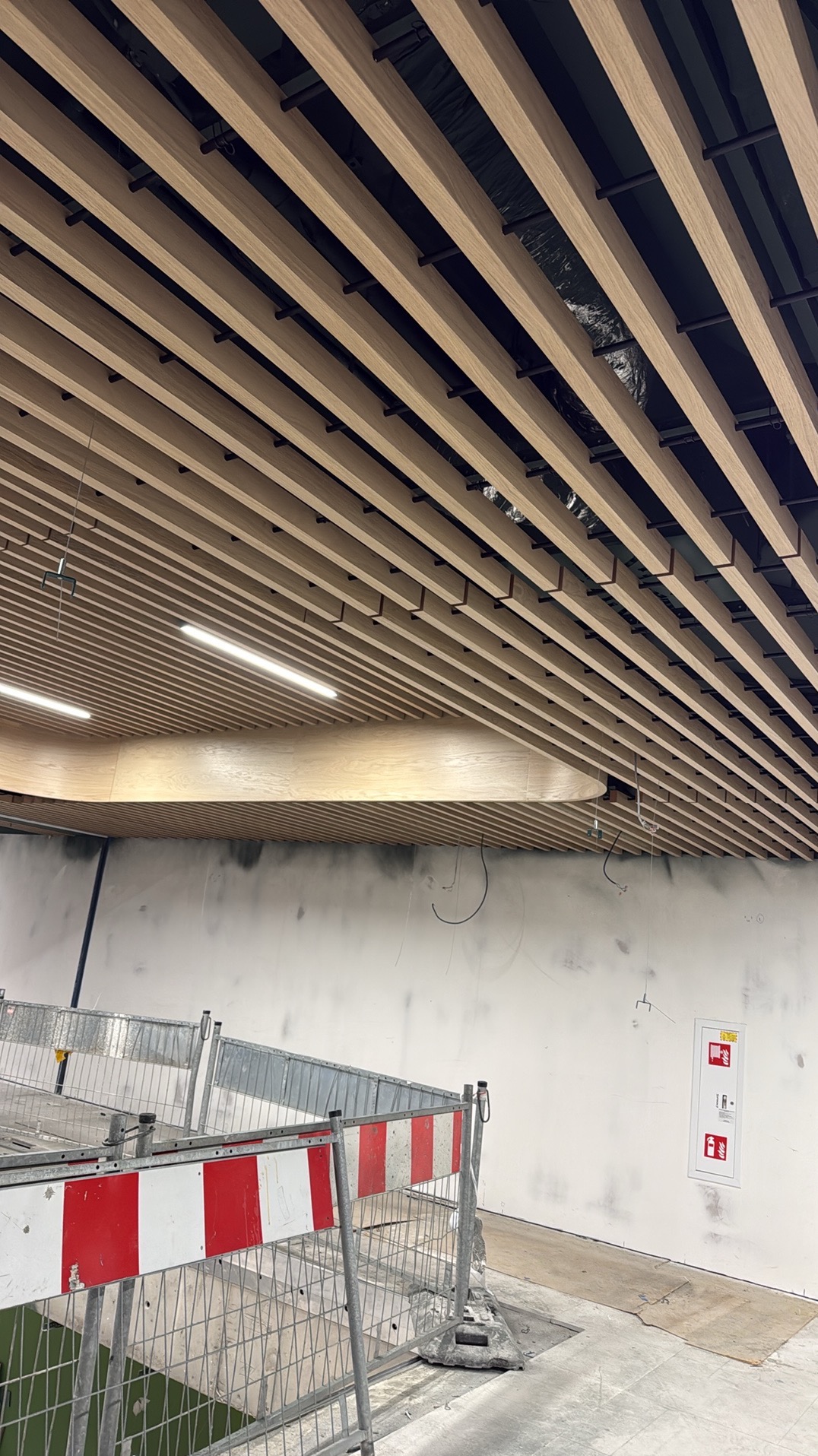 Drewniany sufit lamelowy z oświetleniem liniowym w trakcie montażu, widoczne elementy konstrukcyjne i zabezpieczenia budowlane.