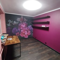 Karol Krankowski - Pokój po odświeżeniu: ciemna podłoga, ściana w kolorze fuksji z półkami, ściana z fototapetą w kwiaty. Na pierwszym planie stół z akcesoriami.