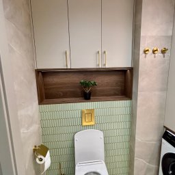 PK-BUD Paweł Kamiński - Nowoczesna łazienka po remoncie: beżowe płytki imitujące marmur, zielona mozaika, wisząca toaleta z złotymi akcentami i szafka z drewnianą wnęką.