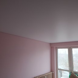 Artlight - Różowe ściany po malowaniu w pokoju z grzejnikiem i oknem balkonowym. Widoczny fragment podłogi i karton. Świeżo pomalowane ściany w pastelowym odcieniu.