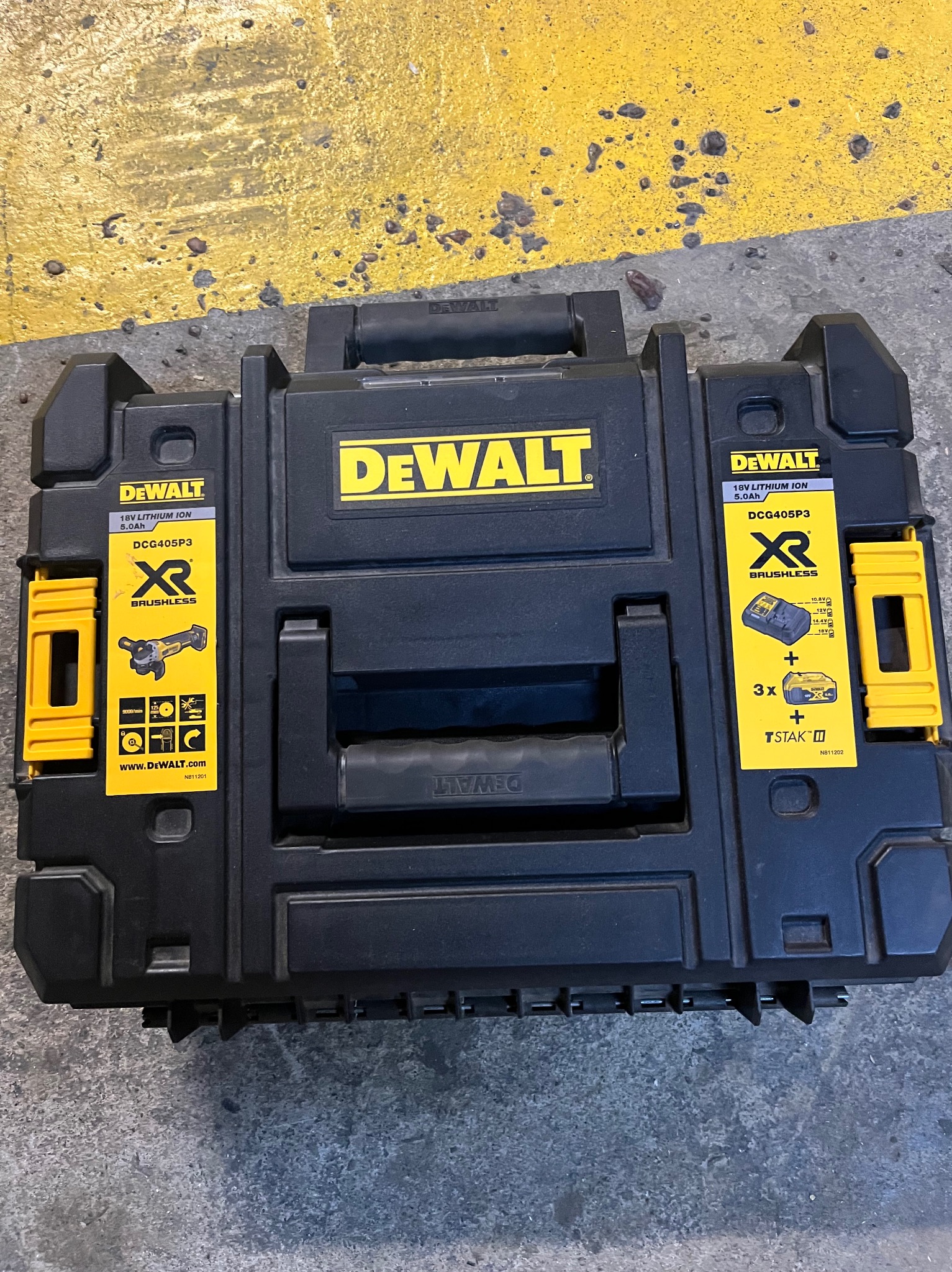 Czarna skrzynka narzędziowa DeWalt TSTAK z naklejkami informacyjnymi na żółtym i szarym tle. Widok z góry, centralne ujęcie.