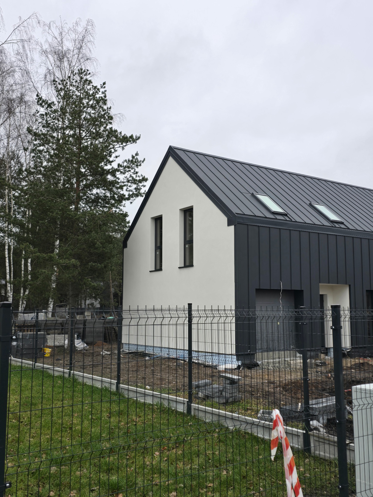 Nowoczesny dom jednorodzinny z grafitową elewacją i dachem w Radzyminie. Widoczne okna dachowe i ogrodzenie panelowe. Minimalistyczny design.