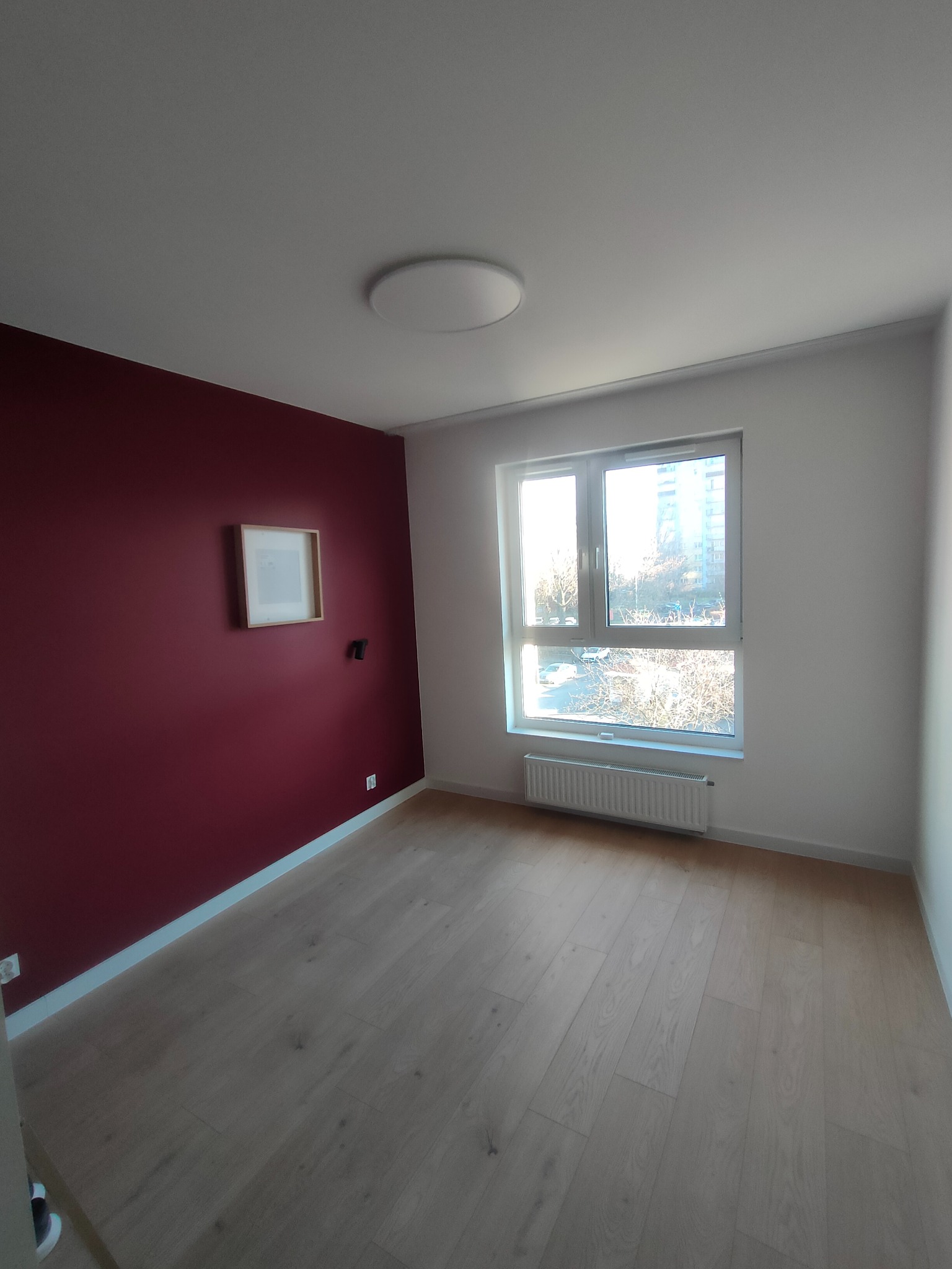Pomieszczenie po malowaniu ścian i ułożeniu parkietu w Wistce. Jedna ściana bordowa, reszta biała. Na ścianie obraz w ramie. Jasna podłoga, okno z grzejnikiem.
