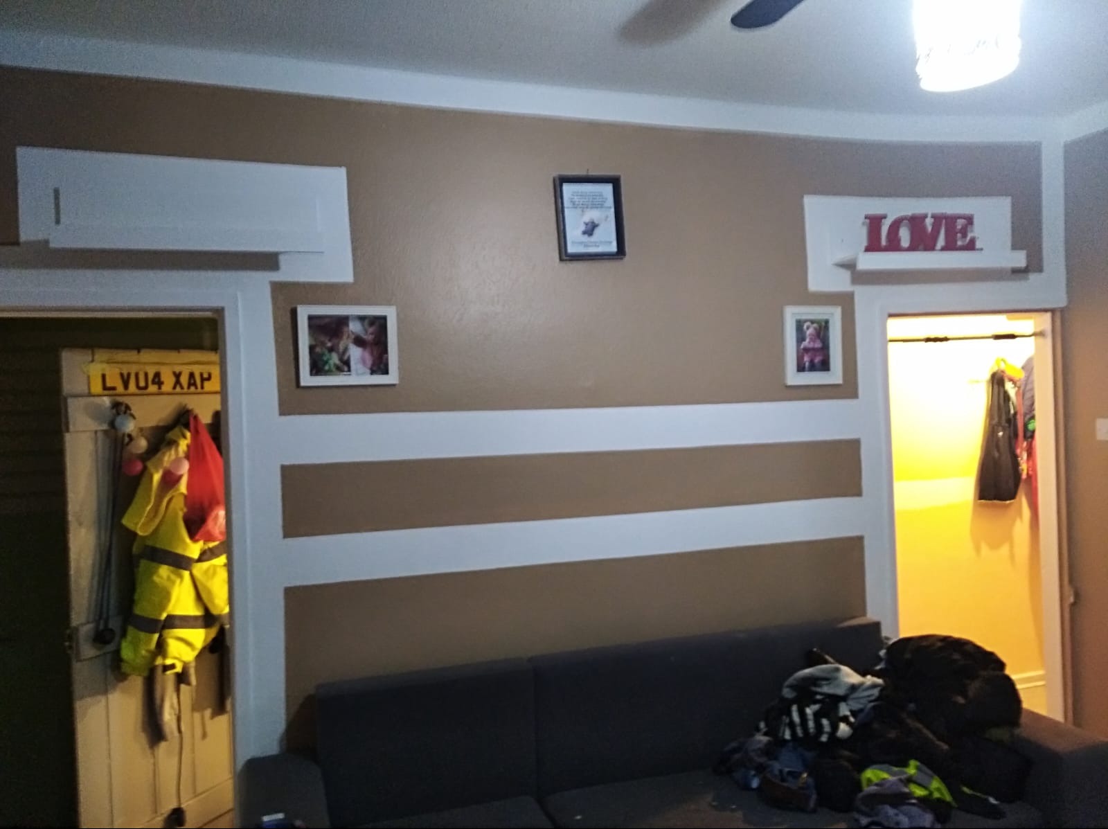 Pokój z brązowo-białymi pasami na ścianie, dekoracjami i meblami. Widoczne drzwi z wieszakami i ubraniami. Oświetlenie sufitowe. Ujęcie z dołu.