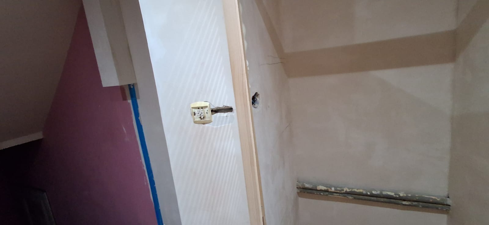 Wnętrze w trakcie prac wykończeniowych: ściana z instalacją elektryczną, fragment ściany pomalowanej na fioletowo, widoczne ślady po remoncie, surowy stan.