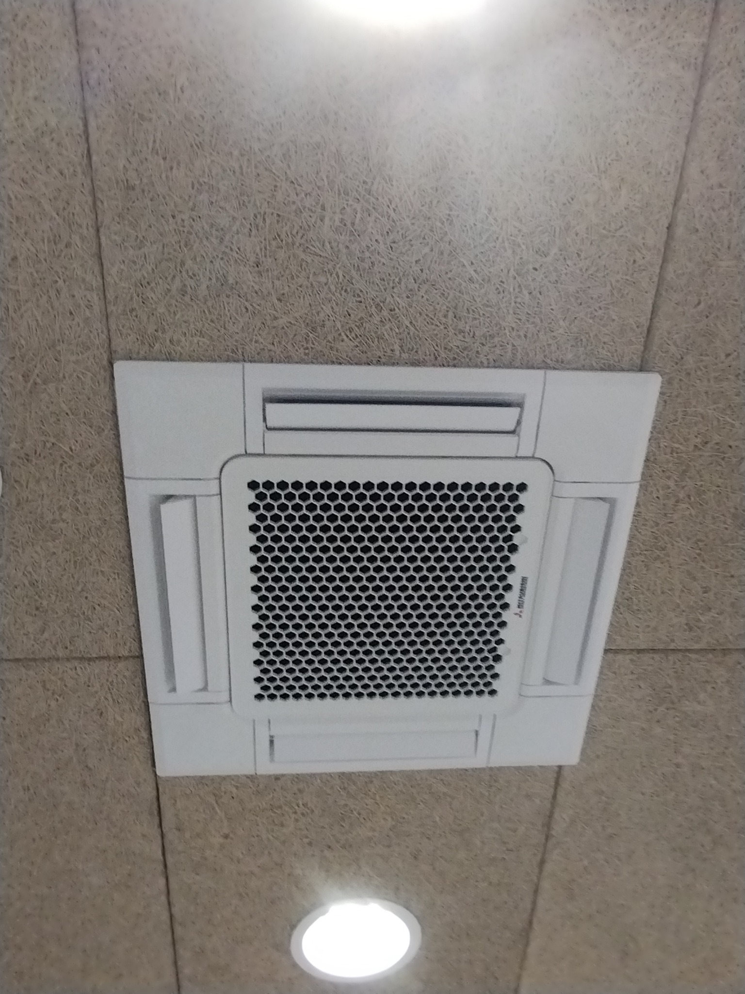Kasetonowa klimatyzacja Mitsubishi Electric zamontowana w suficie podwieszanym z widoczną kratką wentylacyjną i oświetleniem LED. Widok z dołu.