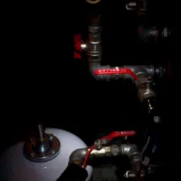 Instalacja hydrauliczna z zaworami Keller i białym zbiornikiem wyrównawczym, widoczna w słabym oświetleniu.