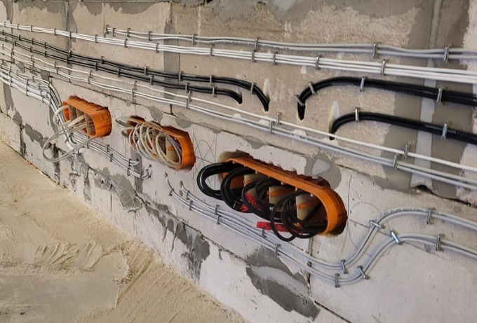 Okablowanie elektryczne w bruzdach ściany z betonu komórkowego, zabezpieczone uchwytami. Widoczne pomarańczowe puszki instalacyjne z przewodami.