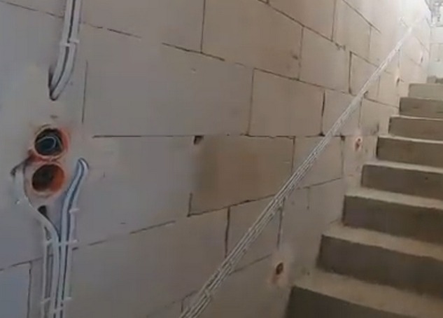 Ściana z betonu komórkowego z zamontowanymi peszlami i puszkami elektrycznymi, widoczne okablowanie. Ujęcie z dołu, w tle schody.