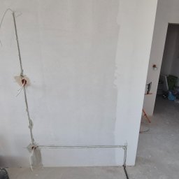 PS-ELECTRO - Ściana w trakcie remontu z poprowadzonymi przewodami elektrycznymi w peszlu i puszkami pod gniazdka. Widoczny sprzęt DeWalt i otwarte przejście do innego pomieszczenia.