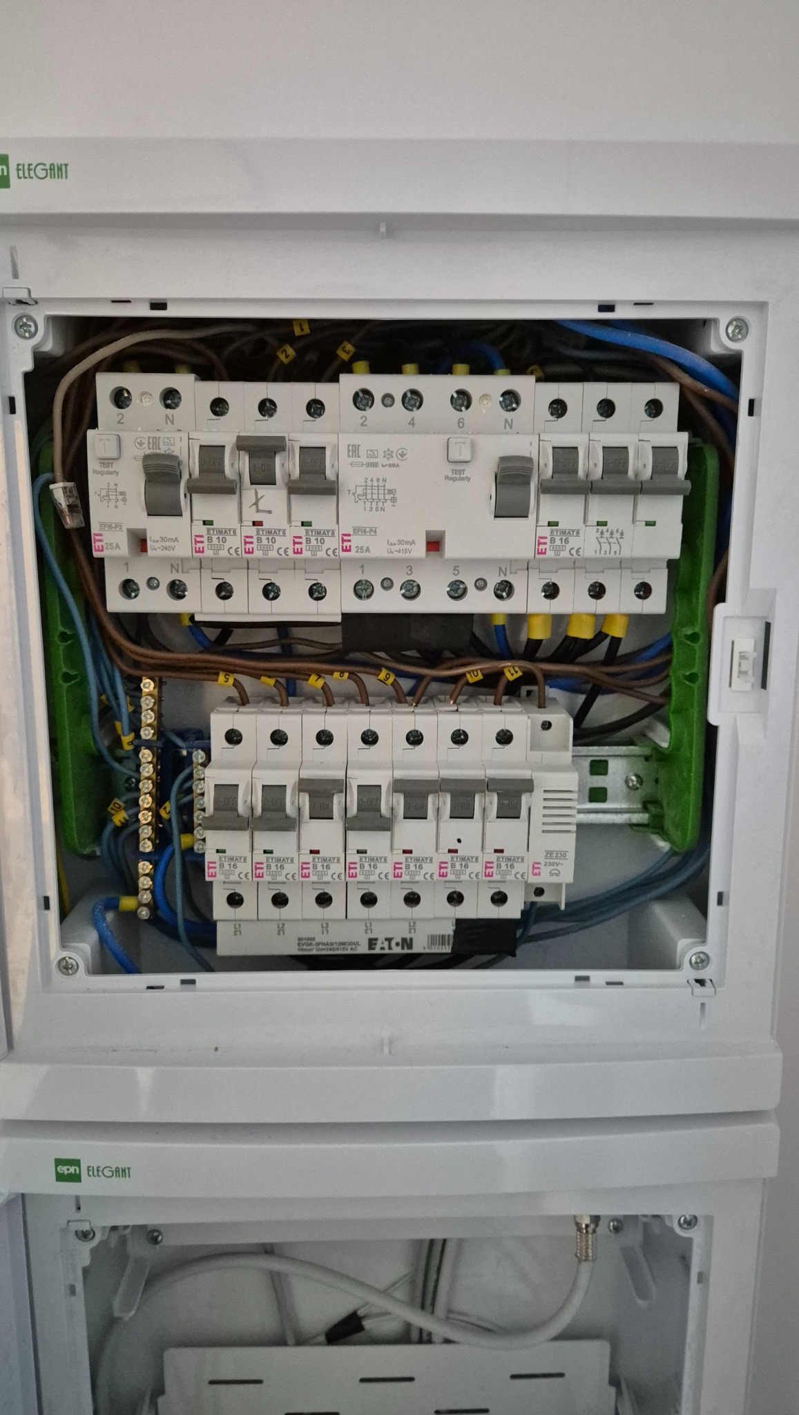 Rozdzielnica elektryczna w białej obudowie, widoczne bezpieczniki, przewody i złączki. Instalacja schludna, z oznaczeniami. Detal montażu wewnątrz budynku.