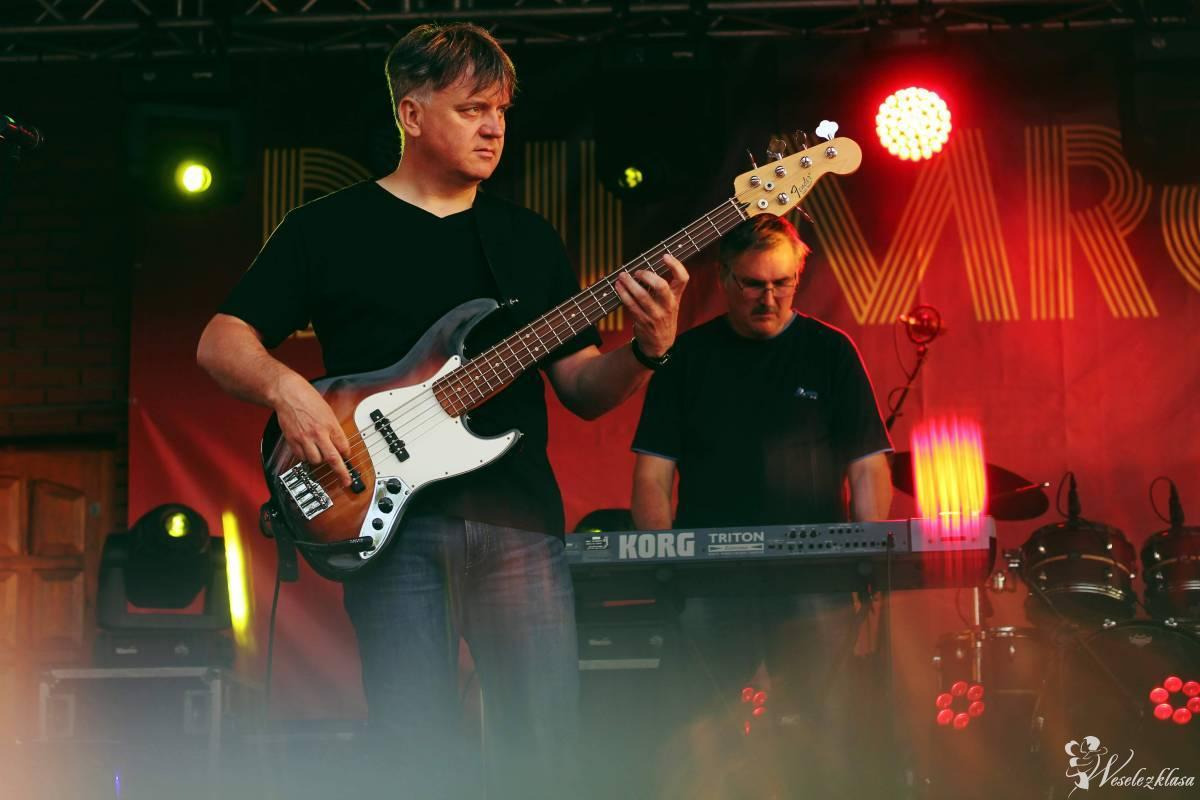 Zespół muzyczny na scenie: basista gra na gitarze basowej, w tle klawiszowiec przy keyboardzie Korg Triton, czerwone oświetlenie sceniczne.