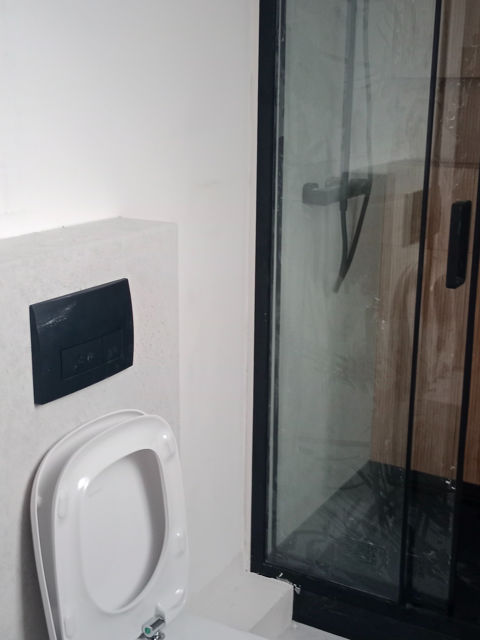 Nowoczesna łazienka: podwieszana toaleta z czarnym przyciskiem spłukującym i kabina prysznicowa z ciemną ramą. Minimalistyczny design, jasne ściany.