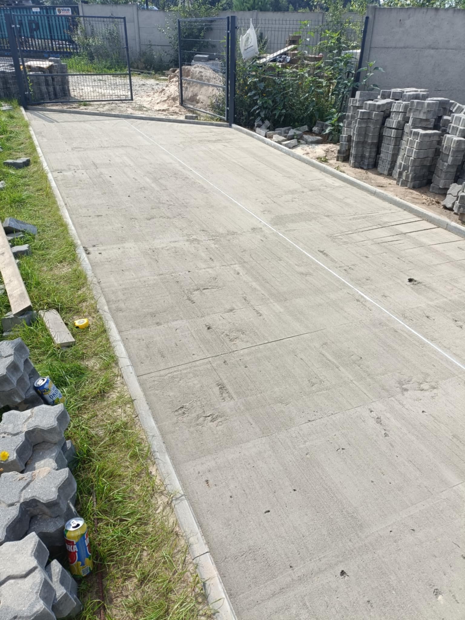 Świeżo wylana, betonowa podbudowa pod kostkę brukową na podjeździe, z widocznymi liniami podziału i przygotowanymi krawężnikami. Częściowo ułożona kostka brukowa.