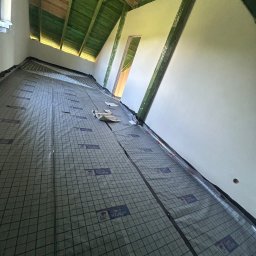 Wiktor Zarzycki - Izolacja pod ogrzewanie podłogowe na poddaszu, widoczne rury instalacji grzewczej. Ujęcie z dołu, perspektywa zbieżna, surowe wykończenie.