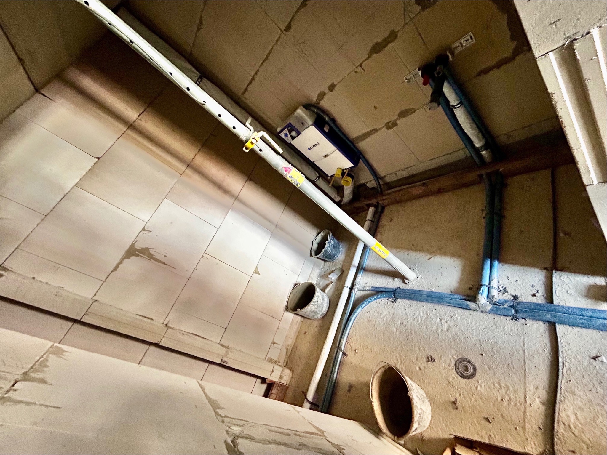 Wnętrze łazienki w trakcie remontu. Widoczne rury instalacyjne, stelaż podtynkowy WC Geberit i narzędzia. Ujęcie z góry, podkreślające etap prac hydraulicznych.