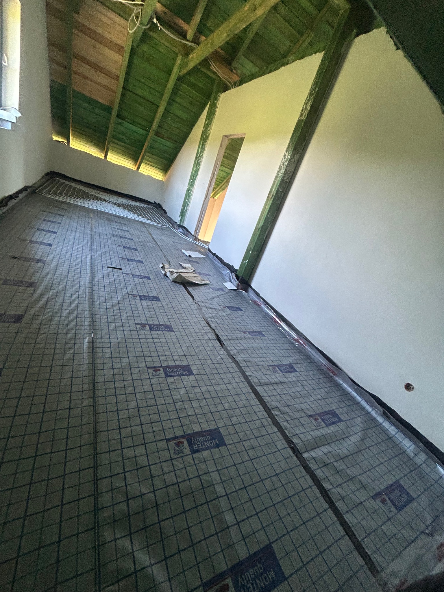 Izolacja pod ogrzewanie podłogowe na poddaszu, widoczne rury instalacji grzewczej. Ujęcie z dołu, perspektywa zbieżna, surowe wykończenie.