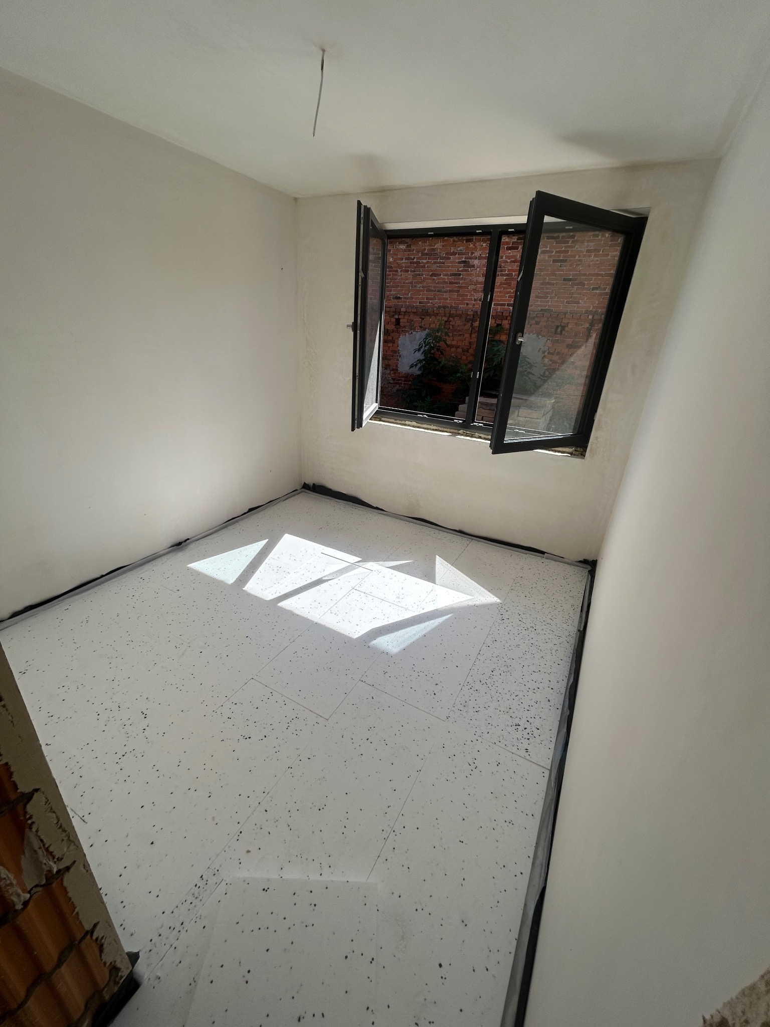 Białe płyty izolacyjne pod ogrzewanie podłogowe ułożone w pokoju z oknem w Bojanowie. Przygotowanie do wylewki. Widok z góry, jasne światło słoneczne.