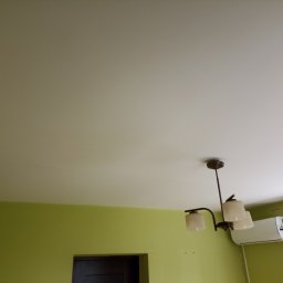 Piotr Bigos - Jasnozielony pokój po malowaniu z białym sufitem, lampą i klimatyzatorem. Widoczny fragment drzwi. Świeżo pomalowane ściany i sufit.