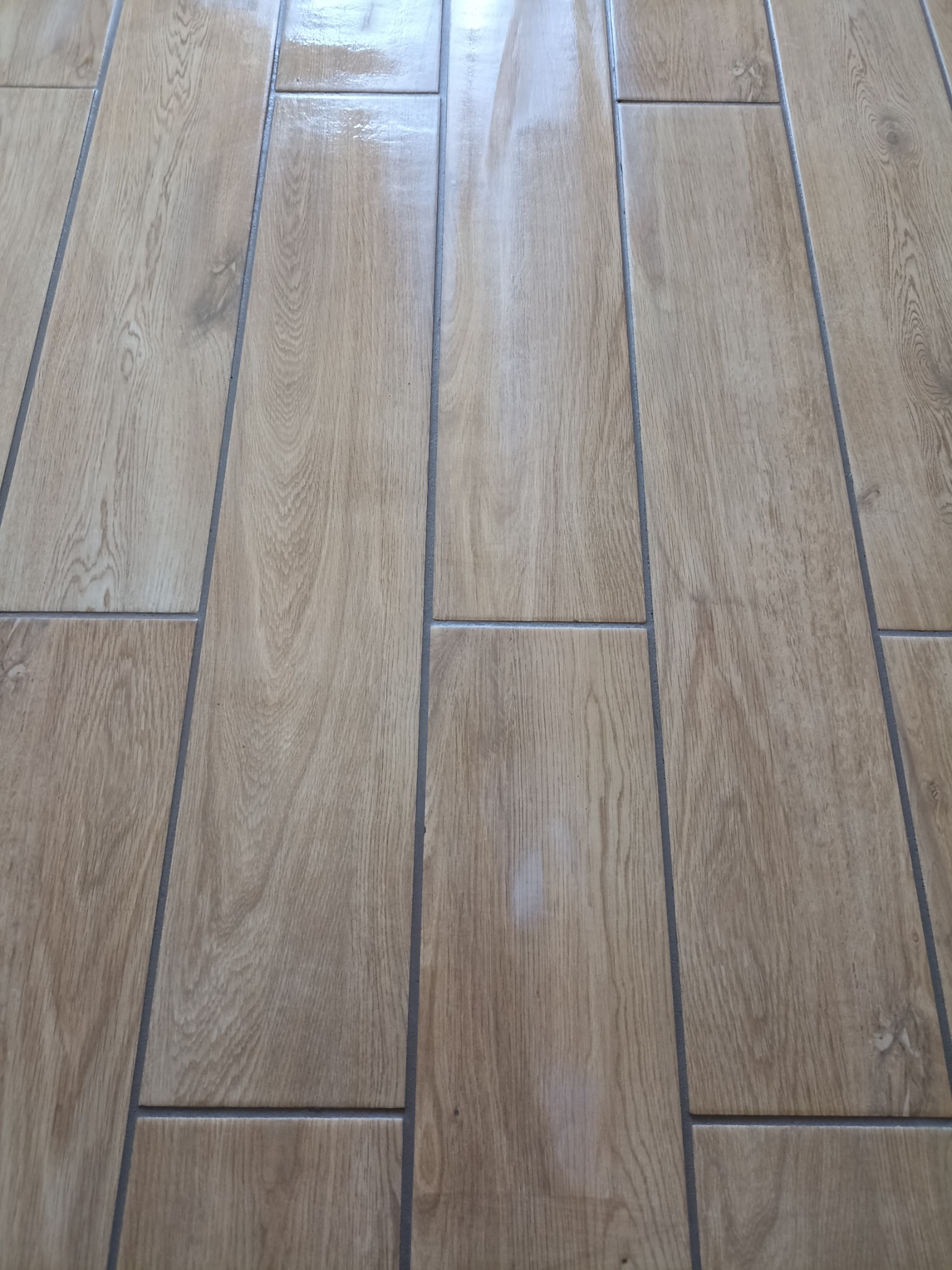 Ułożona podłoga z podłużnych, beżowych płytek imitujących drewno, z ciemnoszarą fugą, widziana pod kątem, z delikatnym połyskiem.